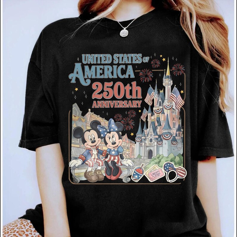 May include: Black t-shirt featuring a colorful graphic celebrating the 250th anniversary of the United States of America. The design includes Mickey and Minnie Mouse, a castle, fireworks, and patriotic imagery.