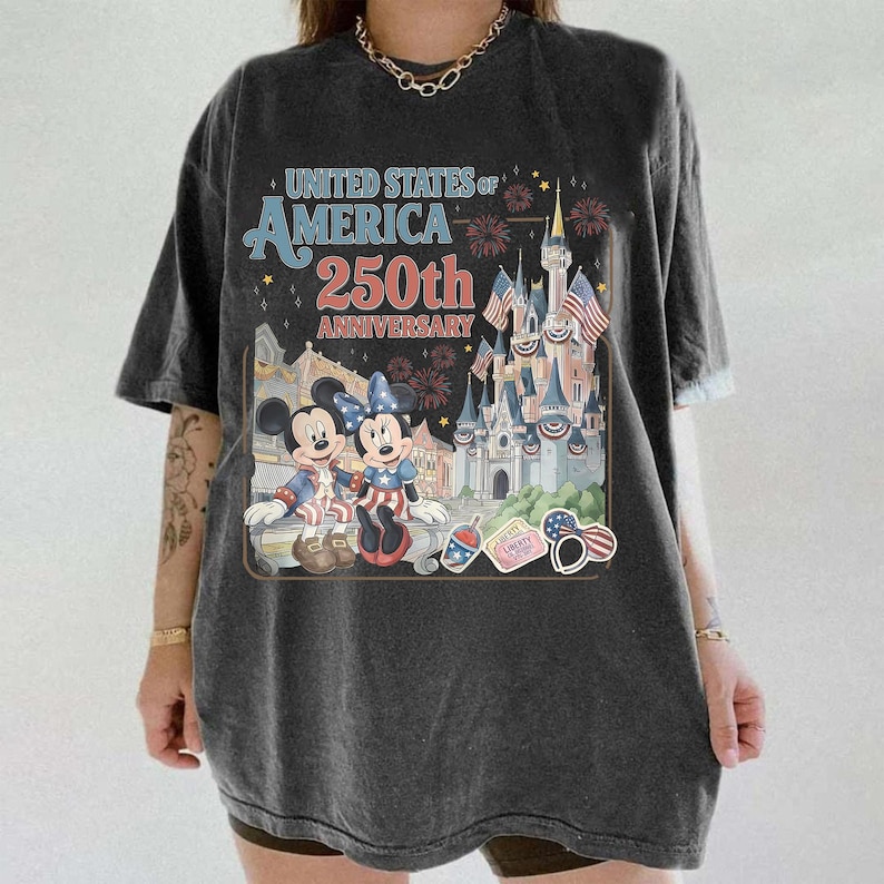 May include: Dark gray t-shirt featuring a graphic commemorating the 250th anniversary of the United States of America. The design includes Mickey and Minnie Mouse, a castle, and patriotic imagery.