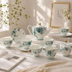 May include: A white porcelain tea set featuring a teal floral pattern with gold trim. The set includes a teapot, multiple teacups with matching saucers, a creamer, and a lidded sugar bowl, all decorated with detailed teal flower illustrations.