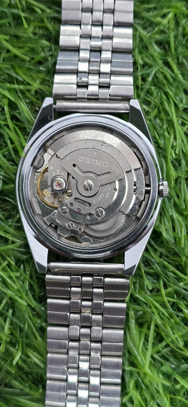 May include: A silver-toned stainless steel wristwatch with an exposed mechanical movement visible through the clear case back. The watch features a metal link bracelet and a circular case with the Seiko brand name engraved on the internal rotor.