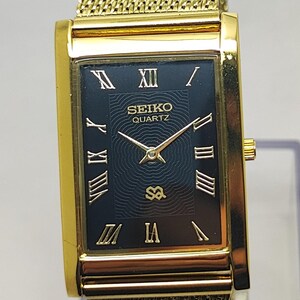 Peut inclure: Montre Seiko Quartz dor&eacute;e avec un cadran noir rectangulaire et des chiffres romains dor&eacute;s. La montre est dot&eacute;e d'un bracelet en maille et d'un bo&icirc;tier dor&eacute;. Le cadran affiche le logo Seiko Quartz et l'heure.