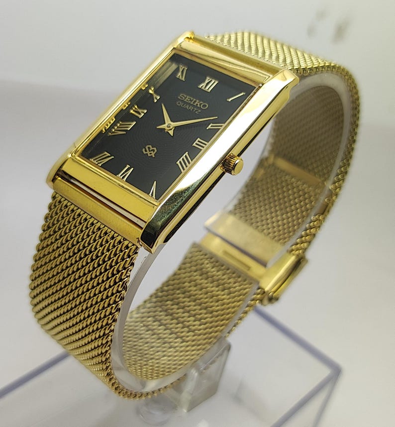 Peut inclure: Montre Seiko Quartz dor&eacute;e avec un cadran noir rectangulaire et des chiffres romains dor&eacute;s. Le bracelet est en maille et le bo&icirc;tier est dor&eacute;. La montre est pr&eacute;sent&eacute;e en biais.