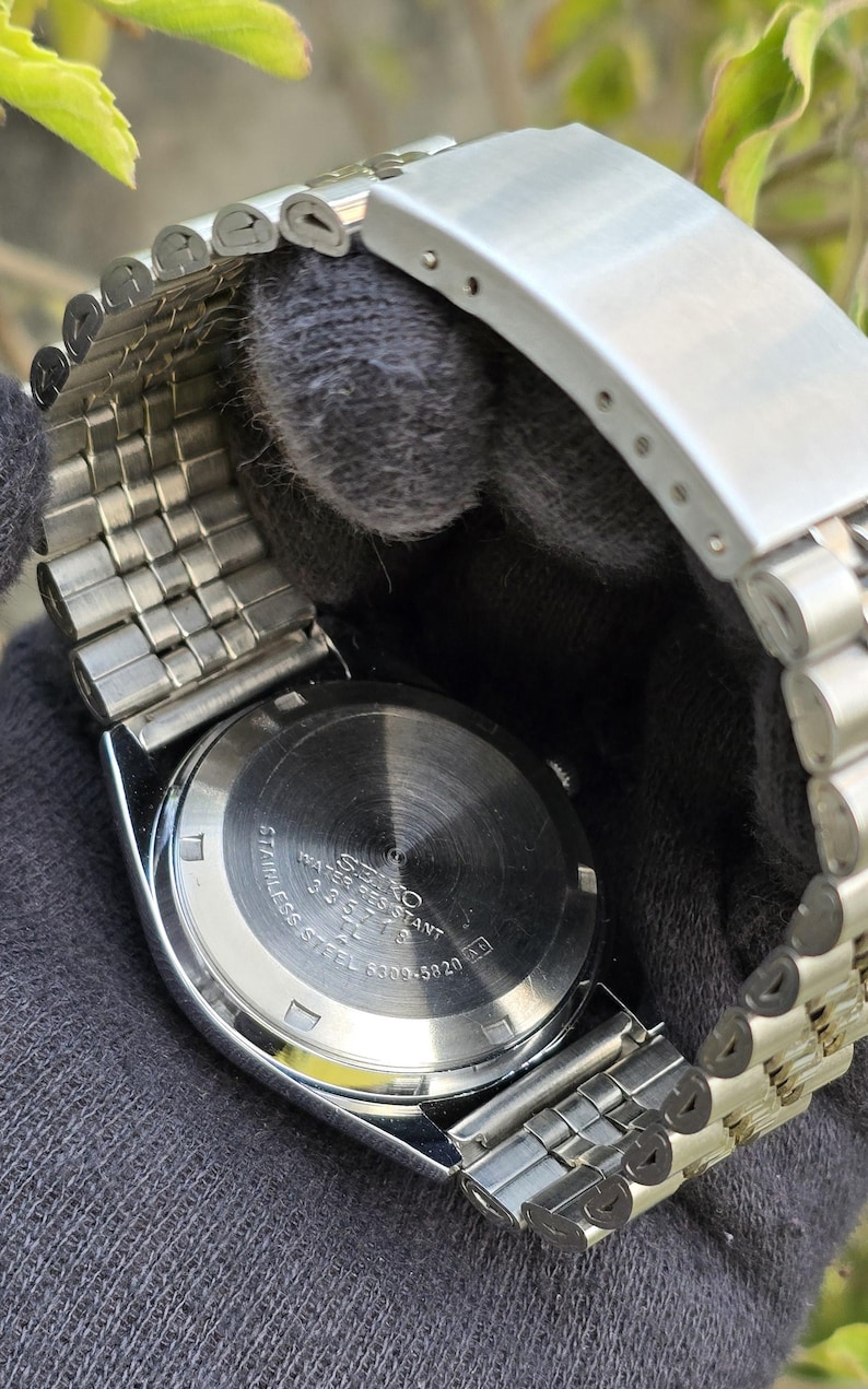 May include: A silver-tone stainless steel wristwatch with a metal link bracelet. The circular case back features engraved text including SEIKO, WATER RESISTANT, STAINLESS STEEL, and the model number 6309-5820, along with a serial number 335718.