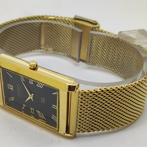 Peut inclure: Une montre Seiko Quartz dor&eacute;e avec un cadran noir rectangulaire et des chiffres romains dor&eacute;s. La montre est dot&eacute;e d'un bracelet en maille dor&eacute;e. Le cadran affiche le logo Seiko et le mot "Quartz".