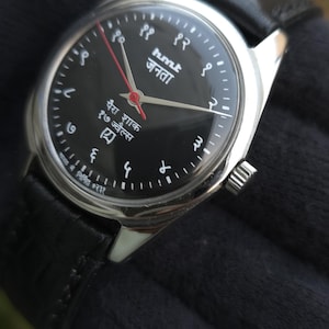 May include: A black analog watch with a silver case and a black leather band. The watch face has white numerals and text in a foreign language. The second hand is red.