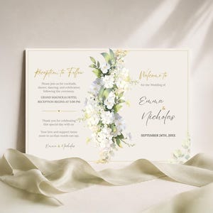 Puede incluir: Una tarjeta de invitación de boda rectangular con un arreglo vertical central de flores blancas y hojas verdes. El texto incluye Reception to Follow, Welcome to the Wedding of Emma & Nicholas y la fecha September 24th, 20XX.