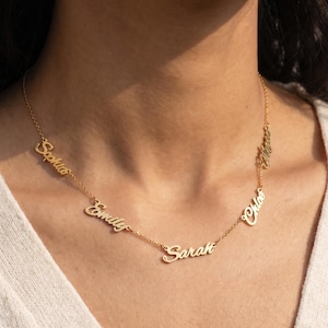 Peut inclure: Un collier doré avec plusieurs pendentifs nominatifs. Les noms "Sophia", "Emily", "Sarah", "Chloe" et "Mia" sont affichés dans une police cursive. Le collier est porté autour du cou.