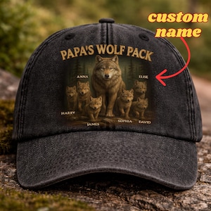 Puede incluir: Gorra de béisbol negra con un diseño de manada de lobos. La gorra muestra el texto "PAPA'S WOLF PACK" sobre una ilustración de un lobo y sus cachorros. También son visibles los nombres "ANNA", "ELISE", "HARRY", "JAMES", "SOPHIA" y "DAVID".