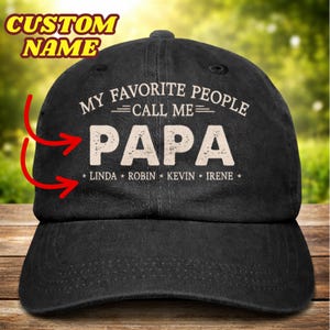 Könnte beinhalten: Schwarze Baseballkappe mit dem weißen Text "MY FAVORITE PEOPLE CALL ME PAPA". Die Namen "LINDA, ROBIN, KEVIN, IRENE" stehen darunter. Auf der Oberseite befindet sich ein Knopf. Die Worte "CUSTOM NAME" stehen oben.