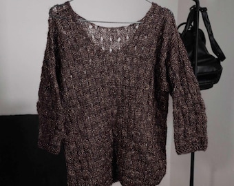 May include: A brown knit sweater with a scoop neck and three-quarter sleeves hangs on a metal hanger. The sweater has a textured pattern and a loose, comfortable fit. The garment is made of a soft, possibly wool or acrylic blend.