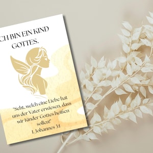 Könnte beinhalten: Eine weiße Karte mit goldenem Text und einer goldenen Illustration einer Frau mit Engelsflügeln. Auf der Karte steht "ICH BIN EIN KIND GOTTES" und ein Bibelvers. Ein Zweig weißer Blätter befindet sich im Hintergrund.
