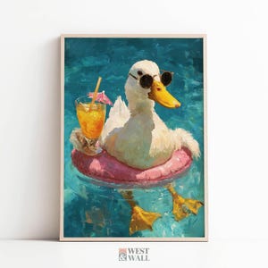May include: A framed art print depicts a white duck wearing sunglasses and a pink inflatable ring, floating in blue water. A cocktail with a straw and umbrella sits nearby. The duck has a yellow beak and feet. The art is signed "West & Wall".