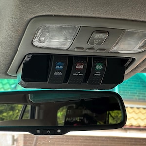 May include: A black overhead console switch panel installed in a vehicle interior, featuring three rocker switches labeled REAR LIGHTS, LED LIGHT BAR, and SIDE LIGHTS, positioned below the factory sunroof controls and above the rearview mirror.
