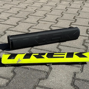 Puede incluir: Dos protectores de cuadro de bicicleta Trek negros y amarillos. El protector negro tiene la palabra "TREK" en relieve. El protector amarillo tiene la palabra "TREK" en negro. Ambos son rectangulares y parecen estar hechos de un material duradero.