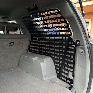 Pode incluir: Barreira de carga de metal preto instalada na parte traseira de um veículo. A barreira apresenta um padrão de grade com aberturas quadradas e é montada no interior do veículo. O interior do veículo é cinza com piso alcatifado.