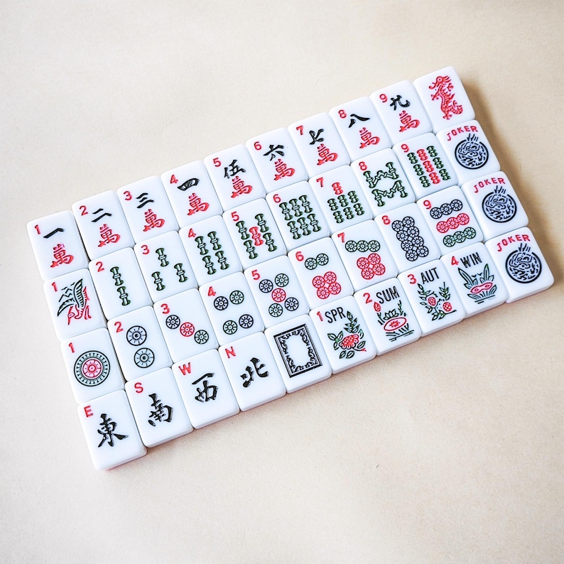 May include: A collection of white rectangular mahjong tiles arranged in a grid. The tiles feature various red, green, and black engraved symbols, including Chinese characters, numeric values, seasonal icons, and joker labels with dragon illustrations.