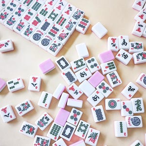 May include: A collection of white Mahjong tiles featuring various red, green, and black engraved symbols, characters, and floral designs. Some tiles are blank with solid pink backs, while others display text like Joker, Win, Sum, Spr, and Aut.
