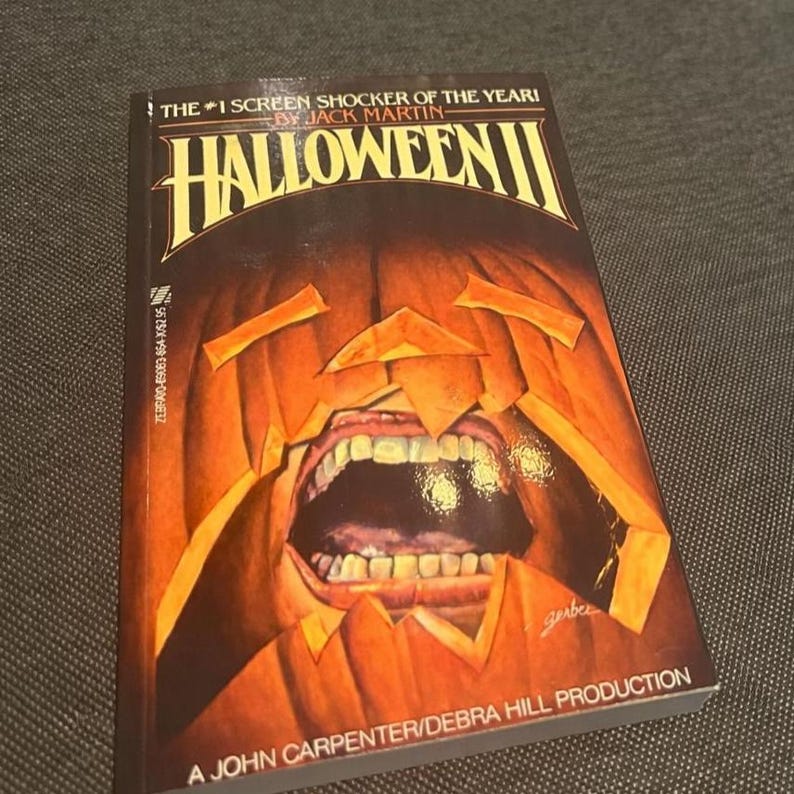 Pu&ograve; includere: Un libro tascabile intitolato "Halloween II" di Jack Martin. La copertina presenta una zucca intagliata con la bocca aperta e i denti. Il libro &egrave; una produzione di John Carpenter/Debra Hill.
