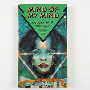 May include: A paperback book titled Mind of My Mind by Octavia E. Butler. The cover features a green and blue illustration of a woman's face with a glowing triangle and a house at the bottom. Text reads: Centuries of genetic mutation gave her the telepathic web—and with it she became the bold and magnetic mistress of human destiny.