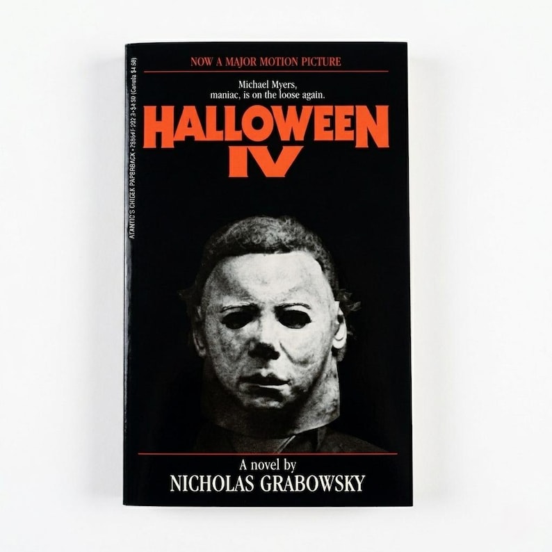 May include: A paperback book with a black cover featuring the title "HALLOWEEN IV" in orange. The cover shows a white mask and the text "NOW A MAJOR MOTION PICTURE". The author's name, NICHOLAS GRABOWSKY, is also visible.