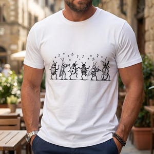 May include: A white short-sleeved t-shirt featuring a black ink-style graphic print of six anthropomorphic insects playing various musical instruments, including a trumpet, violin, and double bass, with small musical notes floating above them.