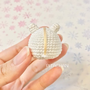 May include: White crocheted amigurumi toy with a yellow stripe down the back. The toy has two small ears on top.