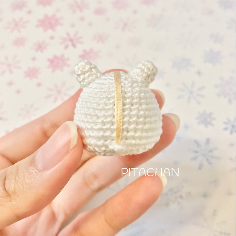May include: White crocheted amigurumi toy with a yellow stripe down the back. The toy has two small ears on top.