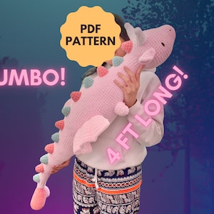 Puede incluir: Un juguete de peluche de dinosaurio de crochet rosa y verde, de 1,2 metros de largo, sostenido por una persona. El texto "JUMBO!" y "PDF PATTERN" son visibles en la imagen.