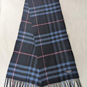 Könnte beinhalten: Ein schwarzer Schal mit einem blau-rosa Karomuster. Der Schal hat eine rechteckige Form mit Fransen an der Unterkante. Ein kleines schwarzes Etikett mit dem weißen Text BURBERRY LONDON ist in der unteren rechten Ecke aufgenäht.