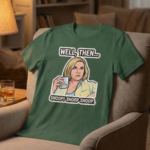 May include: Green t-shirt featuring a graphic of a woman holding a drink, with the text "WELL, THEN..." above and "SHOOPY SHOOP SHOOP." below. The shirt is displayed on a chair in a room.