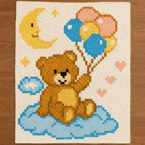 May include: A cross-stitch design featuring a brown teddy bear sitting on a blue cloud and holding colorful balloons. A yellow crescent moon, stars, and pink hearts are also included in the design. The background is off-white.