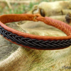 May include: A brown leather bracelet with a black braided design. The bracelet is made with guitar strings.