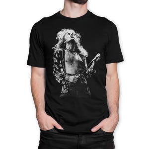以下が含まれることがあります： 黒いTシャツ。長髪のミュージシャンが、柄のジャケットを着てマイクを持っている白黒画像。画像はミュージシャンの上半身のクローズアップです。
