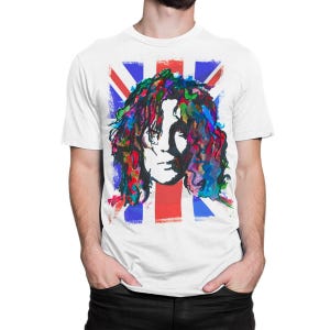 以下が含まれることがあります： ユニオンジャックの背景に、長い髪の人物のカラフルな肖像画が描かれた白いTシャツ。肖像画は、赤、青、緑、紫の鮮やかな色合いの水彩画スタイルです。シャツはクラシックなクルーネックです。