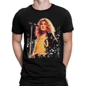 May include: Black t-shirt featuring a vibrant image of a musician with long, wavy hair, standing in front of a microphone. The image has a vintage, artistic style with a splash effect. The shirt is a classic crew neck.
