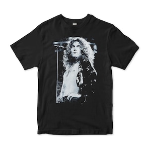 Puede incluir: Camiseta negra con una impresión gráfica en blanco y negro de un cantante con pelo largo y rizado, un micrófono y una chaqueta. La imagen está en la parte delantera de la camiseta.