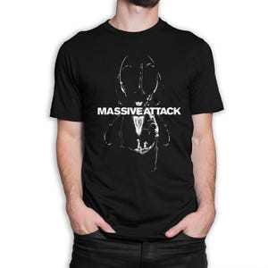 Op de afbeelding: Zwart T-shirt met een witte afbeelding van een insectachtig figuur en de tekst "MASSIVE ATTACK". Het ontwerp is een gedurfde, grafische print op een klassiek T-shirt met ronde hals.