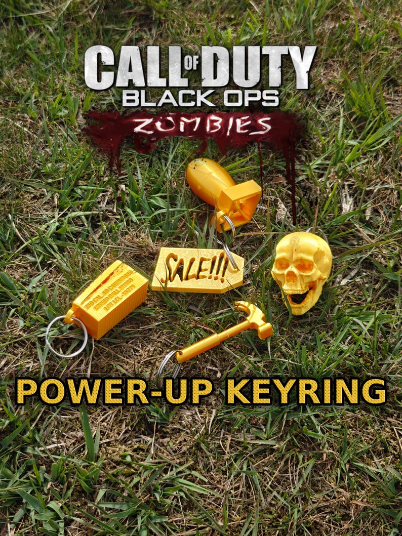 May include: A collection of four yellow keychains featuring a bomb, a skull, a hammer, and a rectangular crate with text, alongside a tag reading SALE!!!. The text CALL OF DUTY BLACK OPS ZOMBIES and POWER-UP KEYRING are visible in the image.