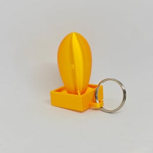 May include: A bright yellow 3D printed keychain featuring a smooth, vertically oriented oval shape attached to a square base. A silver metal split ring is connected to the side of the square base, allowing for attachment to keys or other items.