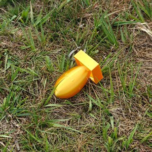 May include: A bright yellow, bomb-shaped keychain featuring a smooth, rounded body and a square-shaped fin assembly at the rear. The object is constructed from a solid, molded material and includes a standard silver-colored metal split ring for attachment.
