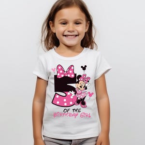 K&ouml;nnte beinhalten: Wei&szlig;es T-Shirt mit einem Minnie Mouse-Motiv, das eine rosa Schleife und ein gepunktetes Kleid zeigt. Die Zahl "5" ist in Schwarz und Rosa gehalten, darunter der Text "OF THE BIRTHDAY GIRL". Das T-Shirt wird von einem jungen M&auml;dchen getragen.