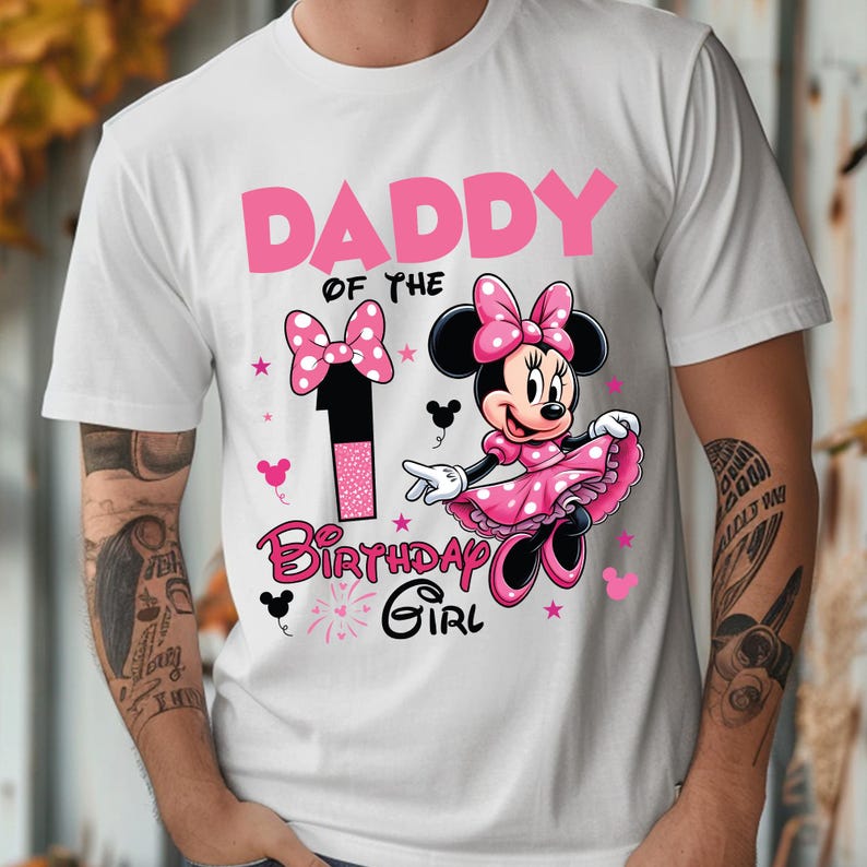 May include: White t-shirt with a pink graphic featuring Minnie Mouse, a number 1, and the text "DADDY of the BIRTHDAY GIRL." Minnie Mouse is wearing a pink dress and bow. The design includes stars and bow accents.