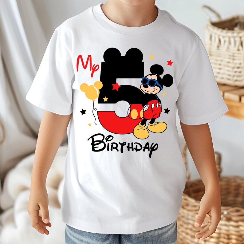 May include: White t-shirt featuring a graphic of Mickey Mouse with sunglasses, the number 5, and the words "My Birthday." The design includes red, black, yellow, and blue elements, with star accents. The shirt is for a child.