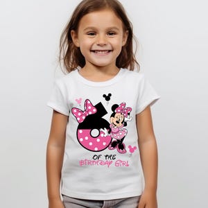 K&ouml;nnte beinhalten: Wei&szlig;es T-Shirt mit der Zahl 6 in Schwarz und rosa Punkten, einem Minnie Mouse-Motiv und dem Text "OF THE BIRTHDAY GIRL" in Rosa. Das T-Shirt wird von einem l&auml;chelnden jungen M&auml;dchen getragen.