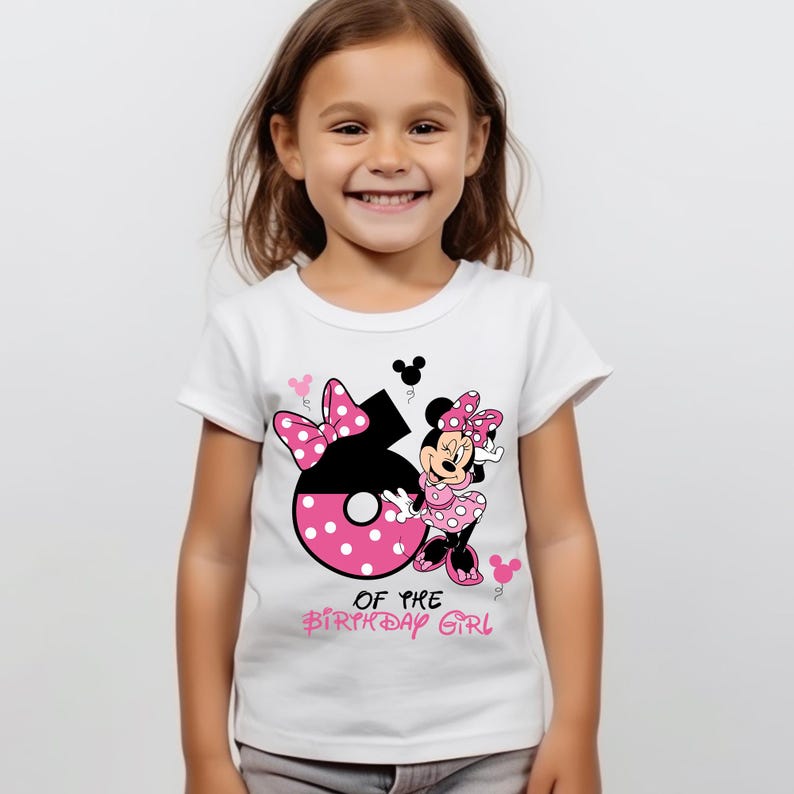 K&ouml;nnte beinhalten: Wei&szlig;es T-Shirt mit der Zahl 6 in Schwarz und rosa Punkten, einem Minnie Mouse-Motiv und dem Text "OF THE BIRTHDAY GIRL" in Rosa. Das T-Shirt wird von einem l&auml;chelnden jungen M&auml;dchen getragen.