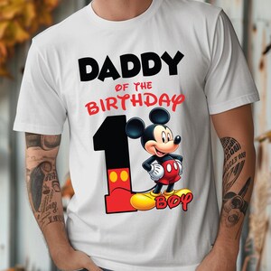 Op de afbeelding: Wit T-shirt met de tekst "DADDY of the BIRTHDAY" in zwart en rood. Een groot nummer "1" staat op het shirt, met Mickey Mouse ernaast. Het woord "BOY" staat in het rood op het shirt.