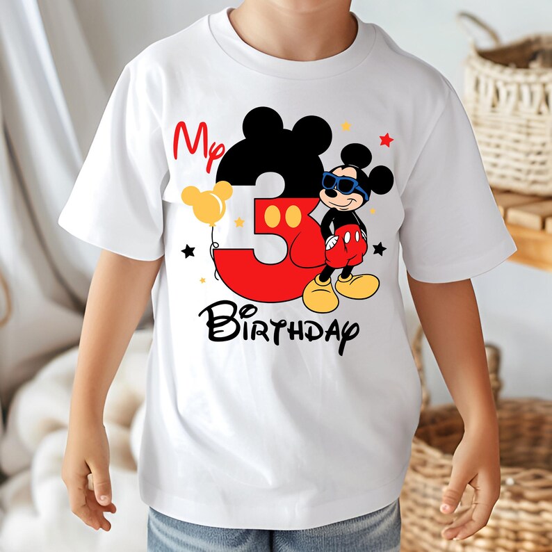 May include: White t-shirt featuring a Mickey Mouse design for a third birthday. The design includes a large red number 3, the words "My Birthday", and a cartoon Mickey Mouse wearing sunglasses. Yellow and black accents complete the design.