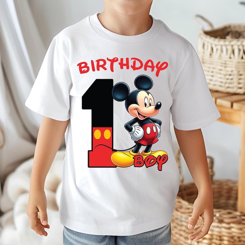 Op de afbeelding: Wit T-shirt met Mickey Mouse, het cijfer 1 en de woorden "BIRTHDAY BOY" in het rood. Mickey Mouse draagt zijn klassieke outfit en staat op het cijfer 1. Het shirt is waarschijnlijk voor de eerste verjaardag van een kind.