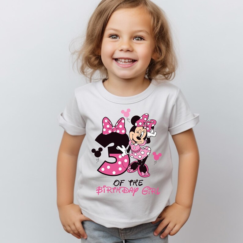 K&ouml;nnte beinhalten: Wei&szlig;es T-Shirt mit Minnie Mouse-Grafik, rosa Schleife und gepunktetem Kleid. Die Zahl "3" ist rosa mit Punkten, und der Text "OF THE BIRTHDAY GIRL" steht darunter in Rosa. Ein Kind tr&auml;gt das T-Shirt.