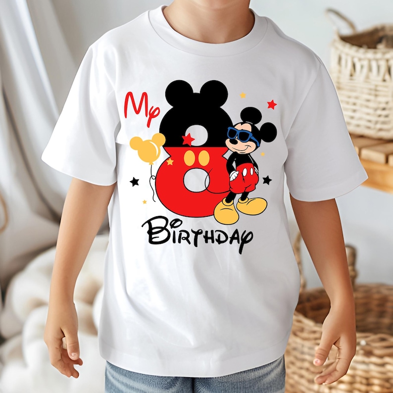 May include: White t-shirt featuring a colorful Mickey Mouse design. The design includes the text "My 8th Birthday" with Mickey Mouse wearing sunglasses. The number 8 is red with yellow balloons and black stars.